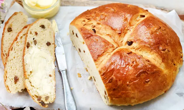 Ein goldbraunes Osterbrot mit Rosinen, aufgeschnitten und mit Butter bestrichen. Perfekt für ein Osterbrot Rezept.