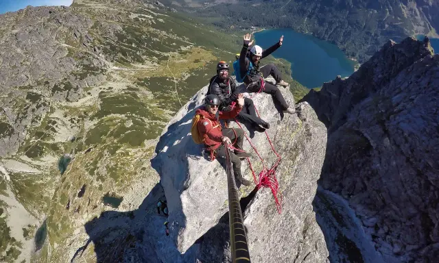 Trzech przyjaciół na szczycie w Tatrach, pozdrawiają z wysokości. Widok zapiera dech w piersiach, jezioro i góry w tle.