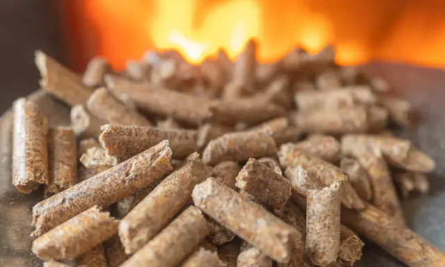 Granulés de bois prêts pour l'installation d'un poêle à granule, avec des flammes chaudes en arrière-plan.