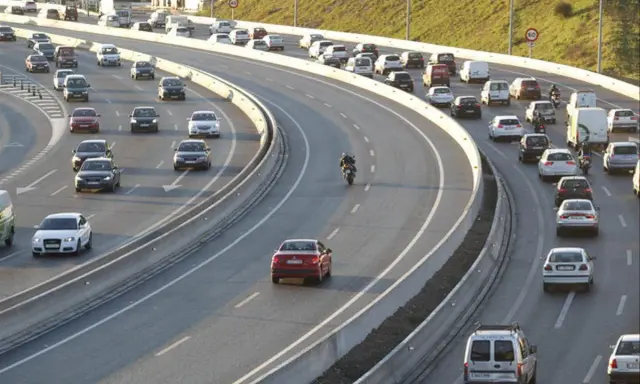 Tráfico intenso en una autopista con varios carriles. Coches, furgonetas y una moto forman la **circulación vao** en un día soleado.