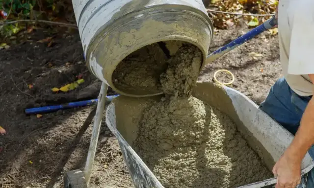 Betoniarka wylewa świeży beton do taczki. Kluczowe jest właściwe proporcje suchego betonu, ile piasku na worek cementu, by uzyskać idealną konsystencję.