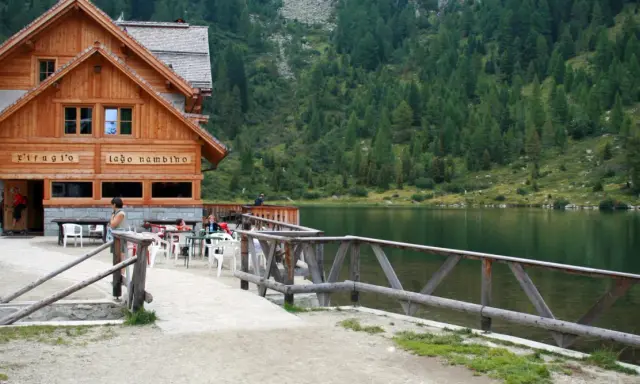 Rifugio sul lago nambino, con tavoli all'aperto e un bosco di conifere sullo sfondo.