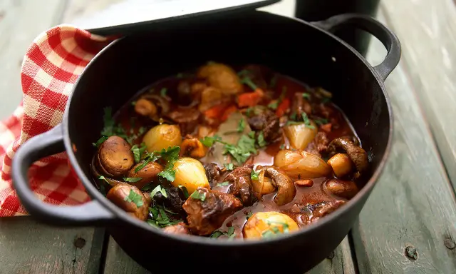 En mustig boeuf bourguignon i gjutjärnsgryta med champinjoner, lök och örter.