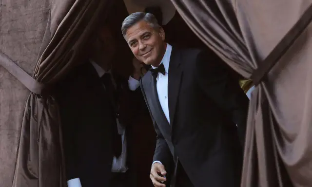 George Clooney, dapper in a tuxedo, emerges from behind velvet curtains. A perfect tix vs suit moment.