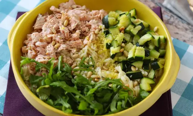 En gul skål med ris, lax, gurka och ruccola. En hälsosam och färgstark måltid.