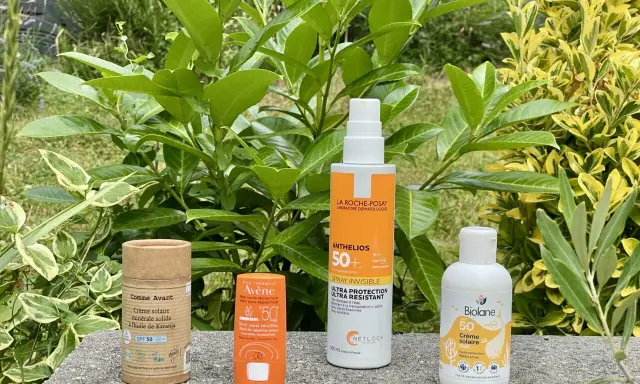 Quatre produits de protection solaire, dont un écran solaire physique, sont alignés sur un muret, entourés de verdure luxuriante.