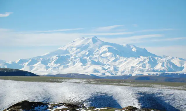 Pokryty śniegiem najwyższy masyw Wielkiego Kaukazu, Elbrus, góruje nad ośnieżonymi wzgórzami i zielonymi dolinami.
