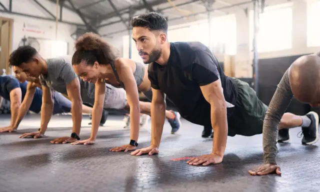 Gruppe trainiert Liegestütze im Fitnessstudio. Ein Mann mit Bart konzentriert sich auf sein ganzheitliches Training.