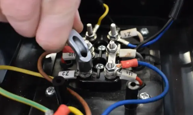 Main d'un technicien manipulant un connecteur sur un bornier électrique. Le moteur électrique chauffe et s'arrête, nécessitant une vérification des connexions.