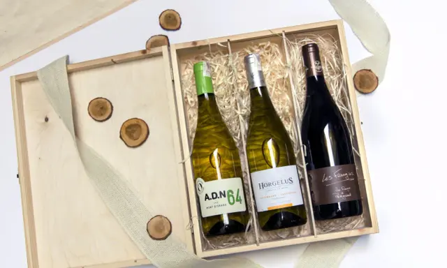 Eleganckie wino w skrzynce na prezent, idealne na wyjątkową okazję. Drewniana skrzynka z trzema butelkami wina, ozdobiona jutową wstążką i drewnianymi krążkami.