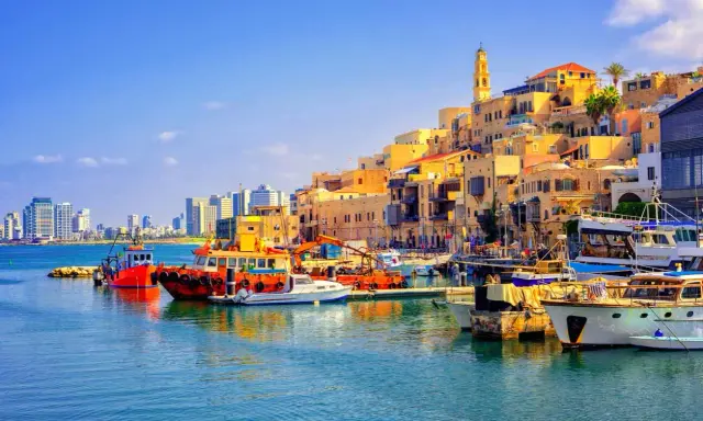 Bunte Boote im Hafen von Tel Aviv, mit der historischen Altstadt im Hintergrund und modernen Hochhäusern am Horizont.