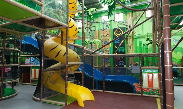Un divertido parque infantil en Madrid con toboganes amarillos y azules, rocódromos y una piscina de bolas.