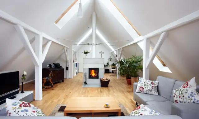 Salon aménagé sous les combles avec cheminée, canapés confortables et poutres apparentes. Le cout d'aménagement combles est bien rentabilisé.