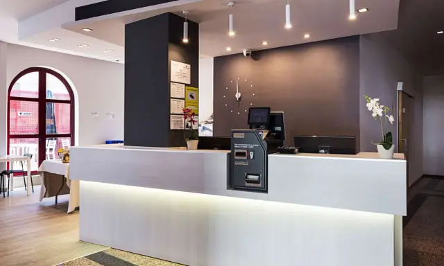 Recepción moderna y luminosa de la residencia Nuevo Versalles, con mostrador blanco, pantalla y máquina de efectivo.