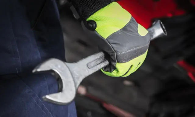 Mano con guante de alta visibilidad, parte de material de protección laboral, sujetando una llave inglesa.