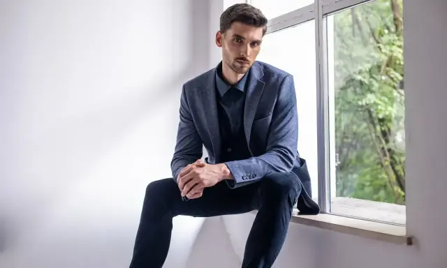 Elegancki mężczyzna w granatowej koszuli i marynarce, zastanawia się, jakie spodnie do niebieskiej koszuli będą najlepsze.
