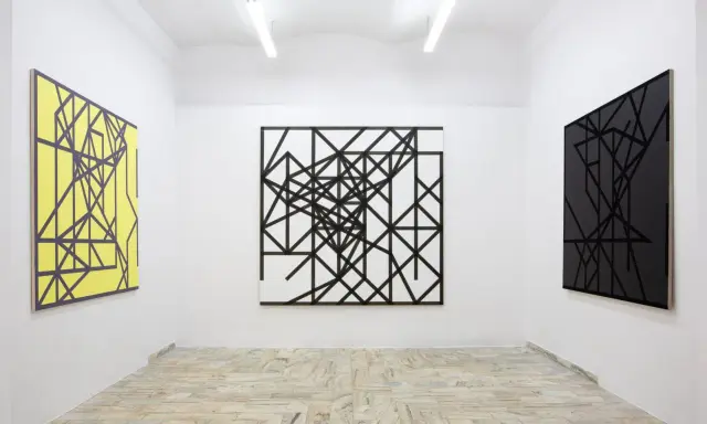 Galeria sztuki z trzema obrazami: żółtym, czarno-białym i czarnym, wszystkie w stylu abstrakcji w malarstwie, z geometrycznymi wzorami.