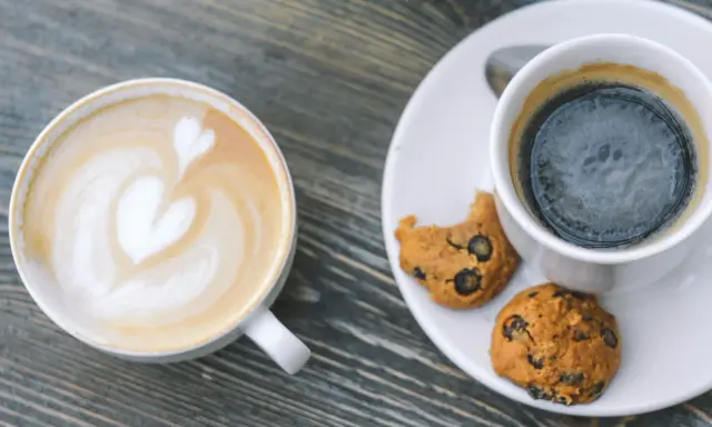 Zwei Tassen Kaffee: ein Latte mit Herz und ein starker Americano mit Keksen.