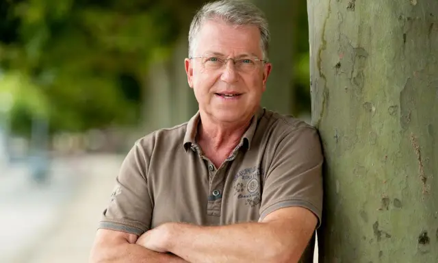 Carsten Sostmeier, ein Mann mit Brille und grauem Haar, lehnt lächelnd an einem Baum.
