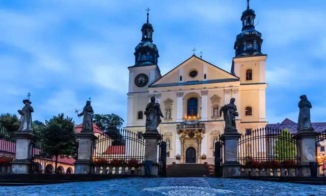 Imponująca bazylika na Kalwarii Zebrzydowskiej, z rzeźbami świętych przed bramą i wieżami w niebo.