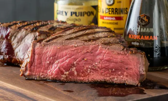 Saftiges, medium-gebratenes Steak mit Grillstreifen, daneben Flaschen für die perfekte Steak Marinade.