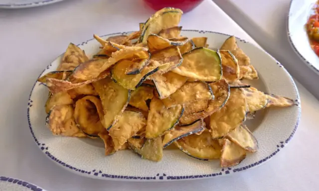 Montón de berenjenas fritas crujientes y doradas en un plato blanco con borde azul. ¡Un aperitivo delicioso!