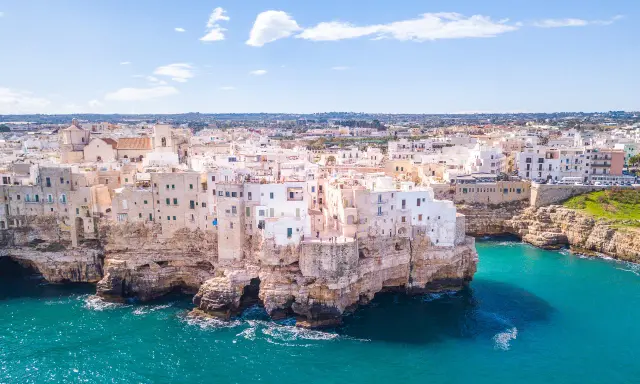 Vista aerea di Polignano a Mare, una delle più belle città da visitare in Puglia, con case bianche aggrappate alle scogliere a picco sul mare turchese.