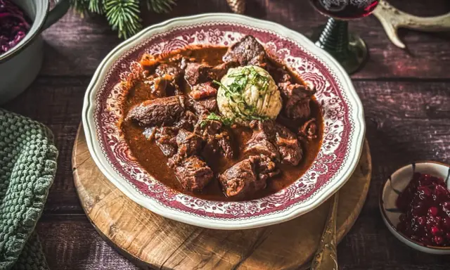 Ein festliches Hirschgulasch, wie es ein Sternekoch zubereiten würde, serviert mit Klößen und Preiselbeeren.