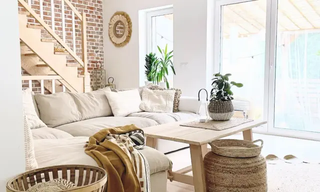 Jasny salon w stylu boho z beżową kanapą, drewnianymi schodami i ceglaną ścianą.