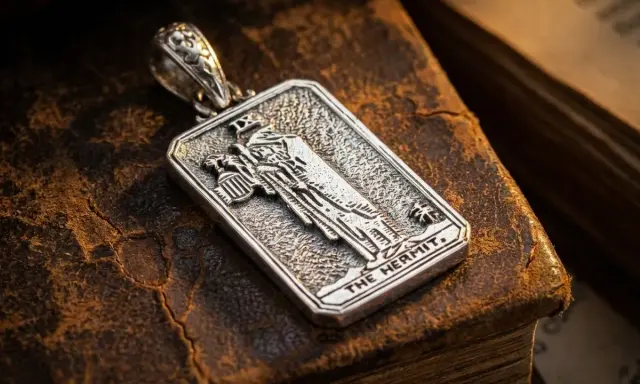 Srebrny wisiorek z motywem pustelnika tarot, leżący na starych księgach.