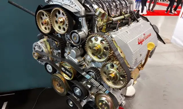 Silnik Alfa Romeo z widocznym układem rozrządu, kołami zębatymi i paskami. Widać napis "GTA 16V" i logo producenta. To serce potężnej maszyny, być może z legendarnym silnikiem hemi.
