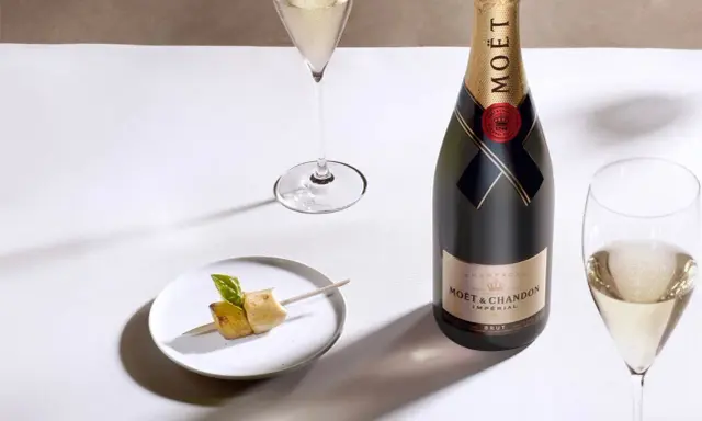 Moët & Chandon Champagnerflasche neben einem Glas Champagner und einem kleinen Häppchen. Das Etikett zeigt das Gründungsjahr, was auf den Degorgierdatum Champagner hinweist.