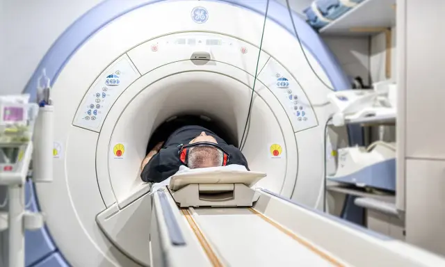 Mężczyzna leży w aparacie do rezonansu magnetycznego, przygotowując się do badania. Jego głowa jest uniesiona na poduszce, a uszy chronią słuchawki. To badanie może pomóc zrozumieć rezonans morficzny.