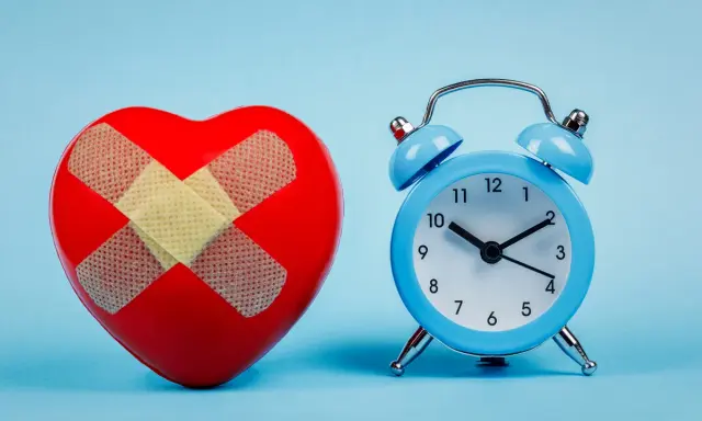 Rotes Herz mit Pflastern und blauer Wecker. Wenn du eine schlaflose Nacht hast, was tun? Zeit für Heilung.