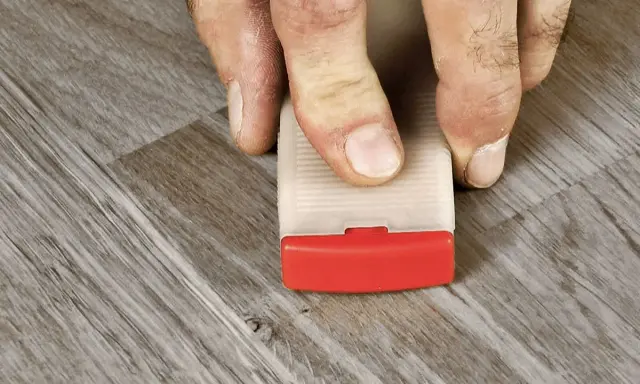 Fingrar trycker ner en kil för att skura laminatgolv.