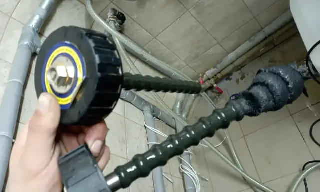 Przygotowanie do czyszczenia instalacji co: ręka trzyma sondę z głowicą do inspekcji rur.