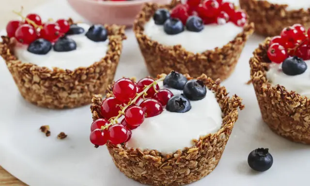 Leckere Granola Cups gefüllt mit Joghurt und garniert mit roten Johannisbeeren und Blaubeeren.