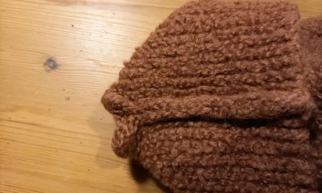 Bruna, sticka tovade tofflor ligger på ett träbord.