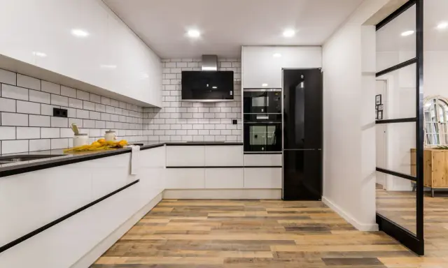 Cocina moderna con pared cocinas mitad azulejo mitad pintura blanca, electrodomésticos negros y suelo de madera.