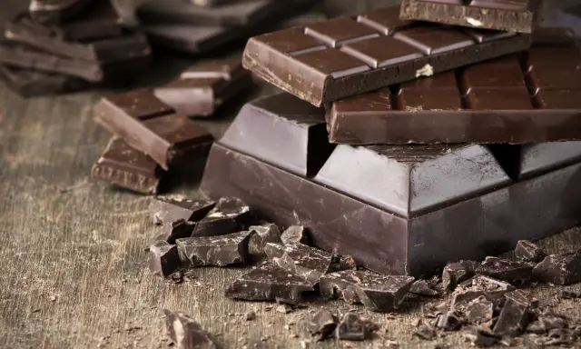 Des morceaux de chocolat noir, entiers et brisés, sur une table en bois. Une invitation à découvrir comment adoucir le chocolat noir pour une dégustation parfaite.