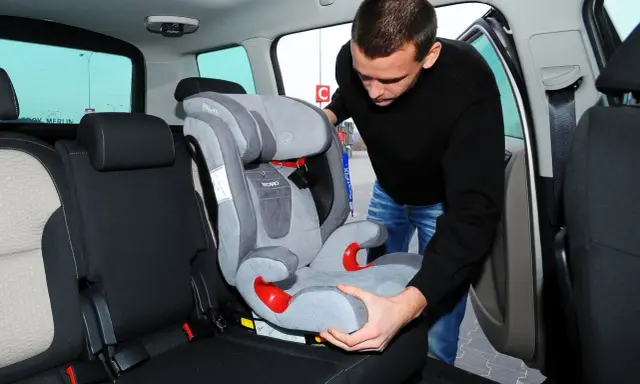 Mężczyzna montuje fotelik dziecięcy, pokazując, jak zamontować isofix w aucie.