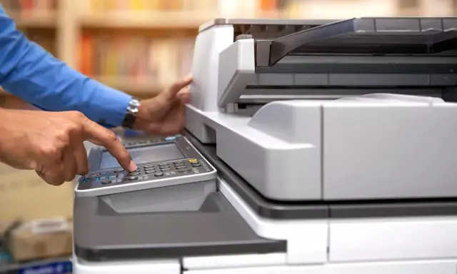 Mani che usano una stampante multifunzione, aiutando a decidere se è meglio stampante laser o inkjet per le proprie esigenze.