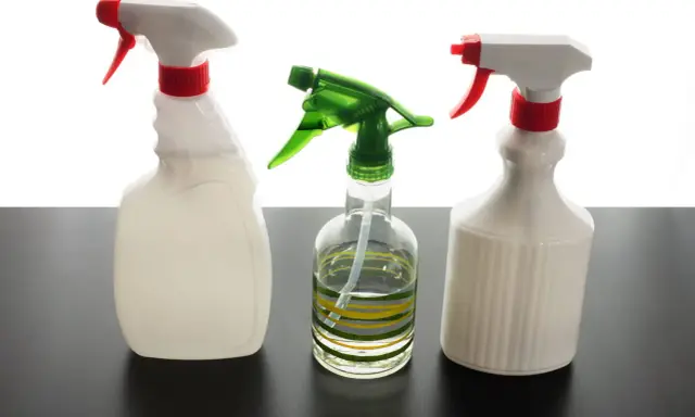 Trois flacons pulvérisateurs, dont un transparent avec des rayures vertes et jaunes, suggèrent un désinfectant naturel pour un nettoyage écologique.