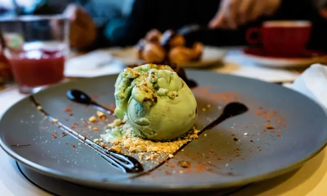 Pyszne lody pistacjowe na talerzu, ozdobione czekoladą i posypką. Idealny deser na poprawę humoru.