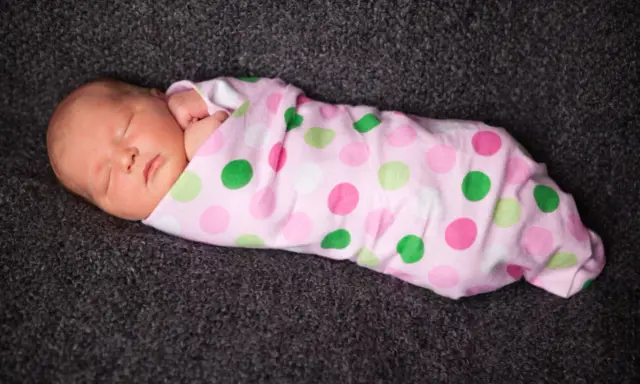 Schlafendes Baby, in rosa gepunktete Decke gewickelt. Pucken ja oder nein? Die süße Kleine scheint es zu mögen.