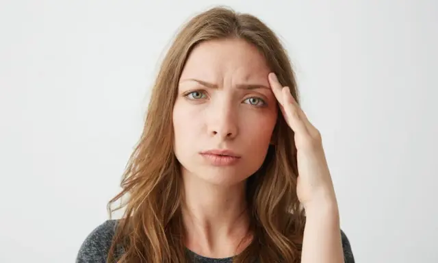 Donna con mano sulla tempia, espressione preoccupata, forse per lo stress ossidativo della pelle.