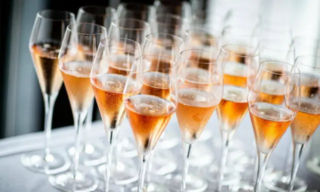 Reihe von Champagnergläsern mit Rosé-Champagner, bereit für den Genuss. So trinkt man Champagner: mit Stil und Freude.