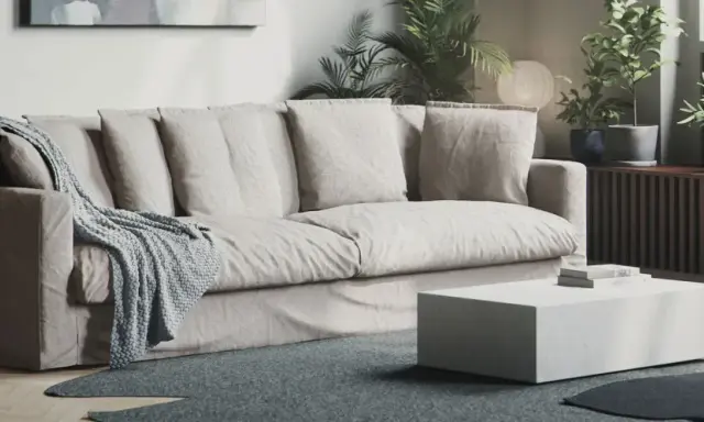 En bekväm soffa med nedsuttna dynor, prydd med en stickad pläd. Framför står ett lågt, vitt soffbord.