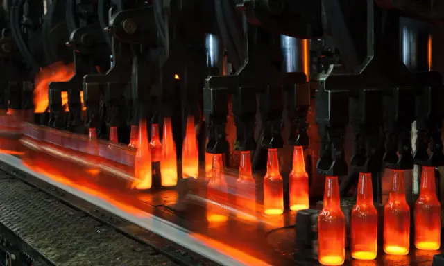Botellas de vidrio al rojo vivo en una línea de producción, un proceso que nos recuerda quién inventó el cristal y cómo ha evolucionado.