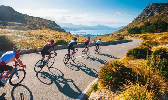 Ciclisti su una strada panoramica, esplorando i più bei percorsi in bicicletta in Italia, con il mare e le montagne sullo sfondo.